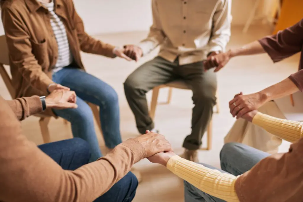 warm toned closeup people holding hands circle therapy session support group copy space