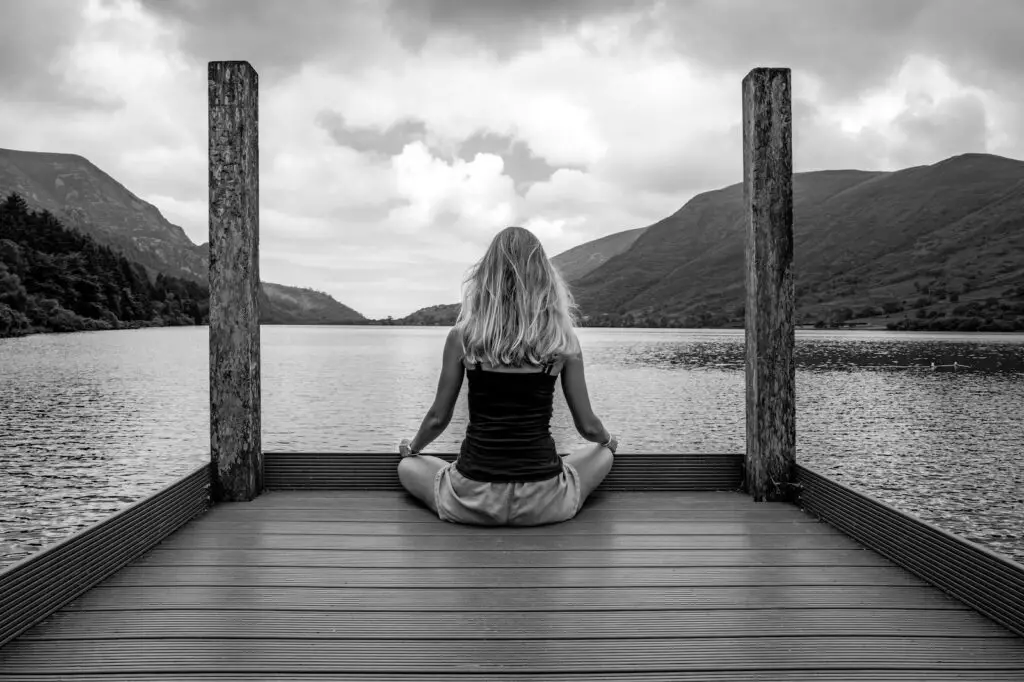 A woman sitting on a dock in front of a body of water