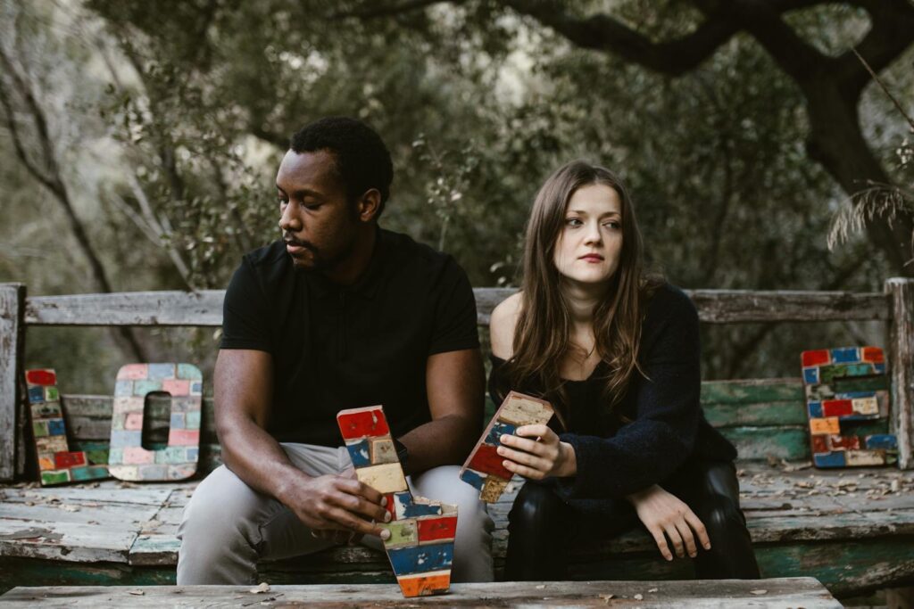 A couple sits in tension on a bench surrounded by nature, holding colorful blocks spelling 'Love'.